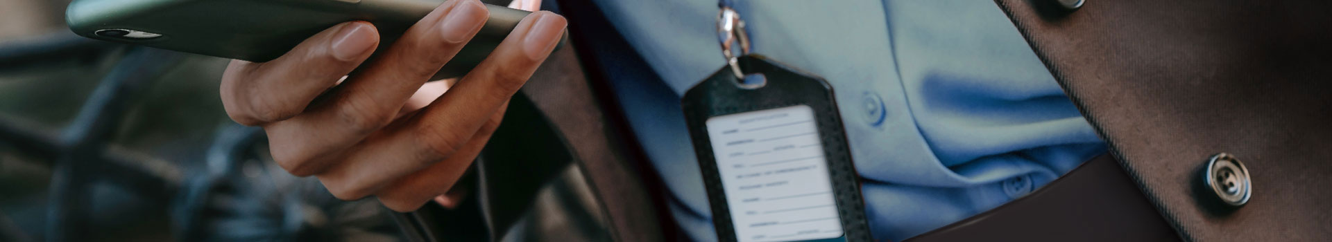 person holding a mobile device wearing an ID badge around neck