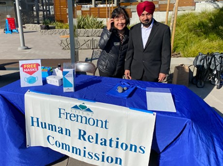 Two Human Relations Commissioners standing in front of a table with a banner that says Human Relations Commission