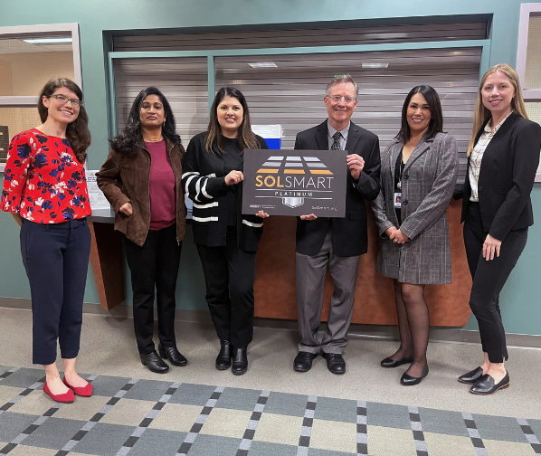 City staff holding SolSmart Platinum Designation signage in City Hall lobby.