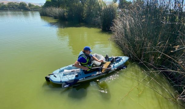 Man fishing out litter from the lake in a kayak.