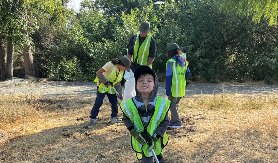 Kid smiling and people picking up litter behind him